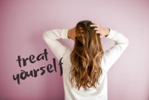 woman with long hair facing away on pink background - text says treat yourself